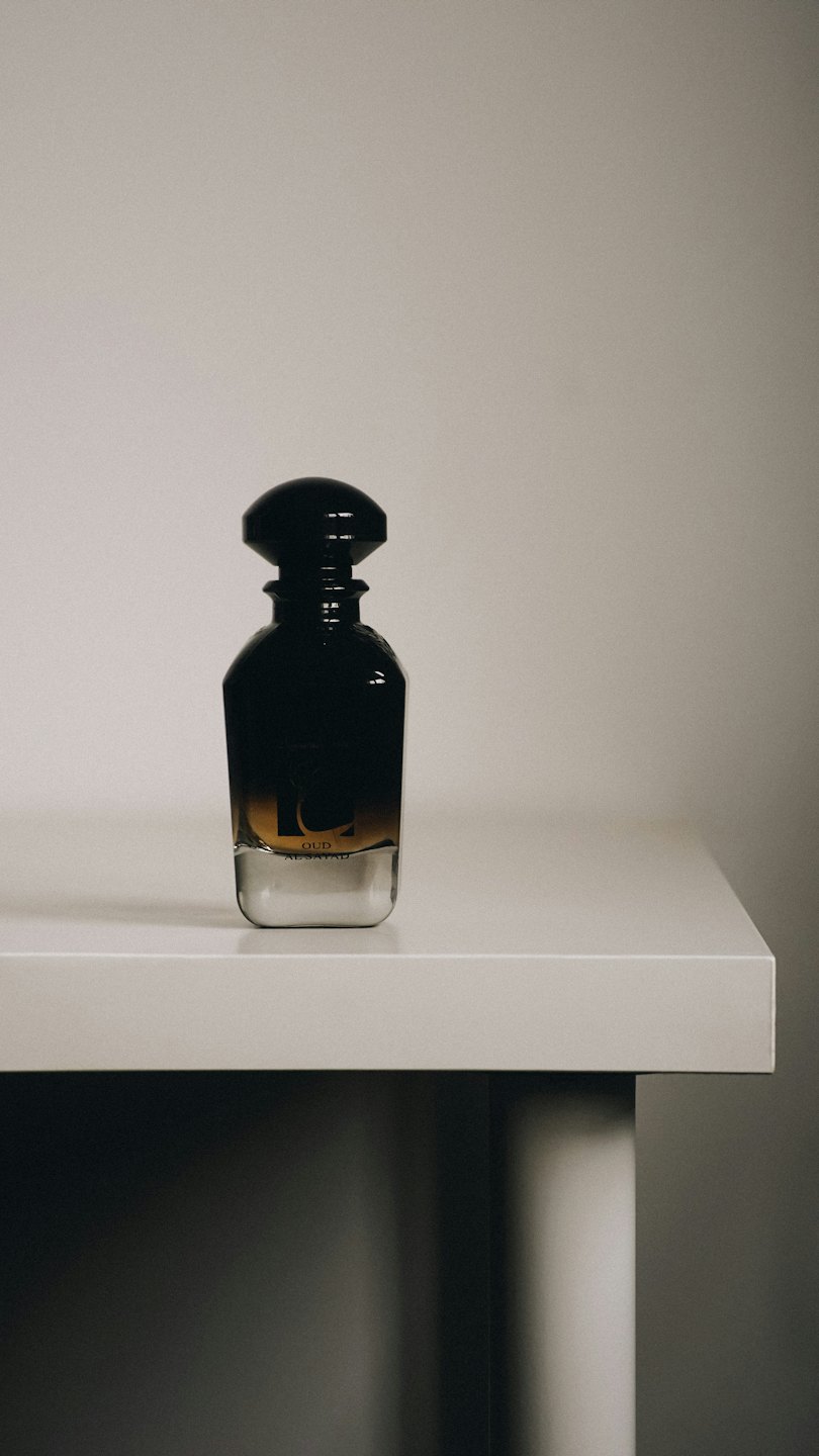 Eleganter Parfumflakon mit bernsteinfarbener Flüssigkeit auf weißer Oberfläche.